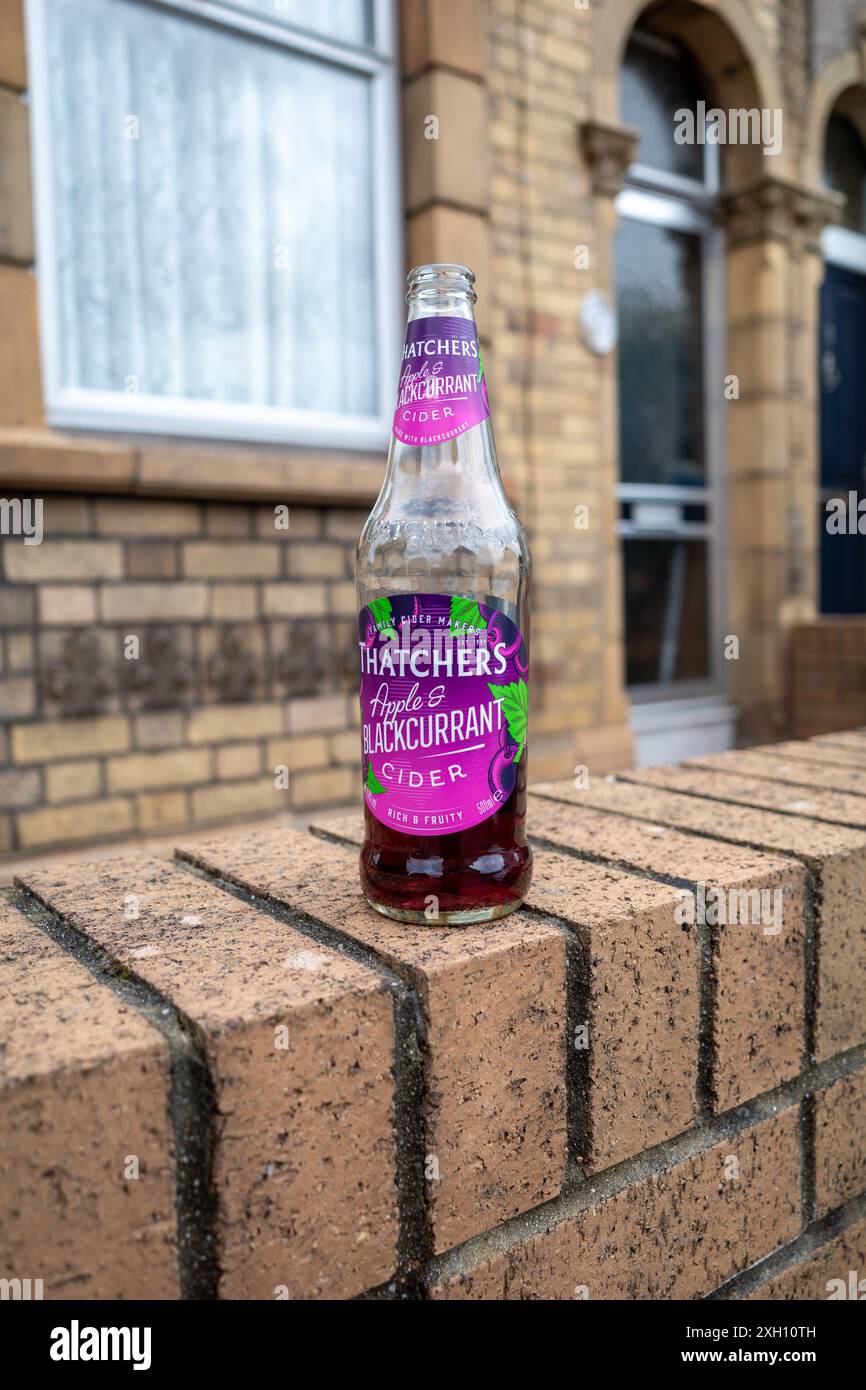 Halb betrunkene Glasflasche Thatchers Apple und Blackcurrant Cider an einer Wand vor einem Haus. Stockfoto