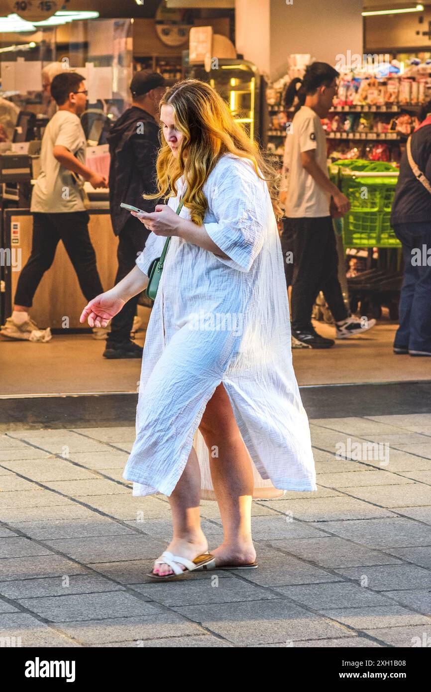 Frau, die lange, lose Nachthemden trägt, geht abends beim Blick auf das Smartphone in der Rue de Rivoli, Paris 75004, Frankreich. Stockfoto