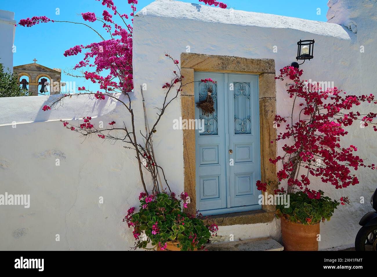 Ein einladendes Gebäude mit einer blauen Tür, umgeben von blühenden Pflanzen, unter hellem Sonnenschein, Chora, Altstadt, Patmos, Dodekanesisch, Griechische Inseln Stockfoto