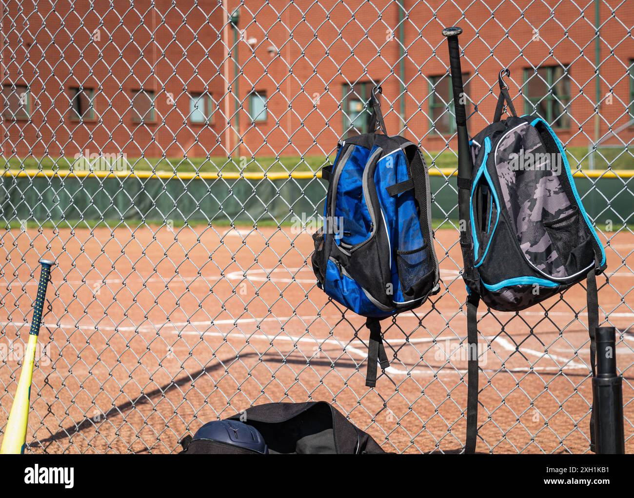 Baseballrucksäcke hängen am Maschendrahtzaun auf dem Little League Baseballfeld Stockfoto