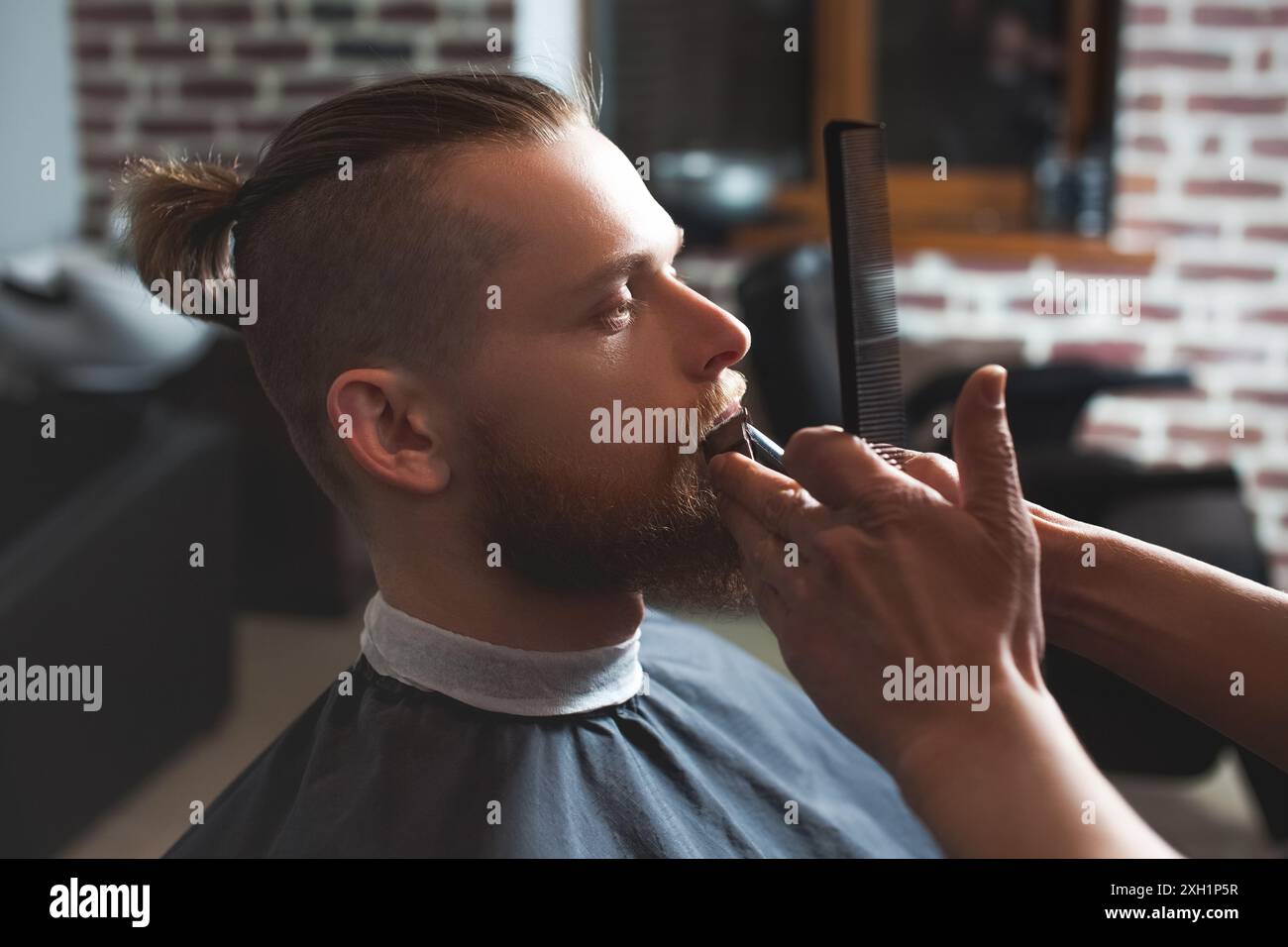 Ein männlicher Friseur auf der Arbeit macht einen Bart und Schnurrbart für einen Mann im Friseurladen. Männliche Kosmetik, Pflege des Barts, für einen stilvollen Look. Stockfoto