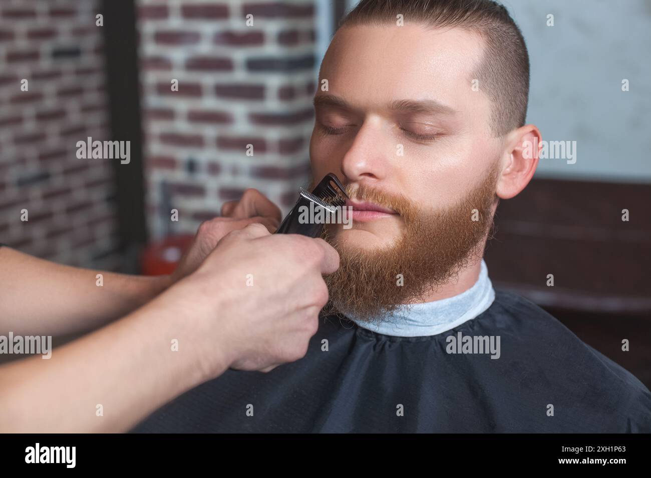 Ein männlicher Friseur auf der Arbeit macht einen Bart und Schnurrbart für einen Mann im Friseurladen. Männliche Kosmetik, Pflege des Barts, für einen stilvollen Look. Stockfoto