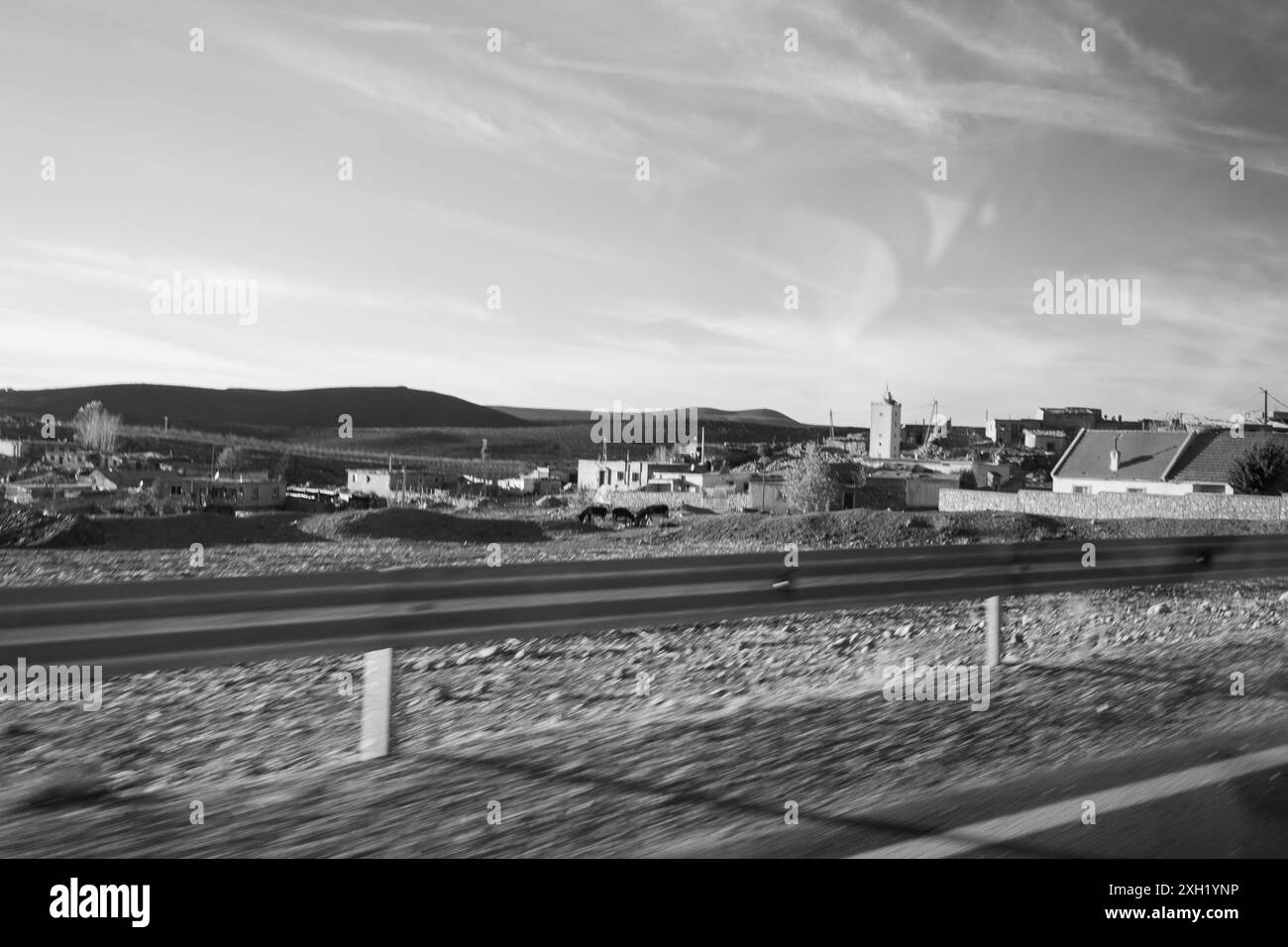 Roadtrip-Szene in Schwarz-weiß, die mit dem Auto auf den Straßen des mittleren Atlas in Marokko unterwegs ist. Du siehst die Bewegung des Autos und eine Stadt mit mir Stockfoto