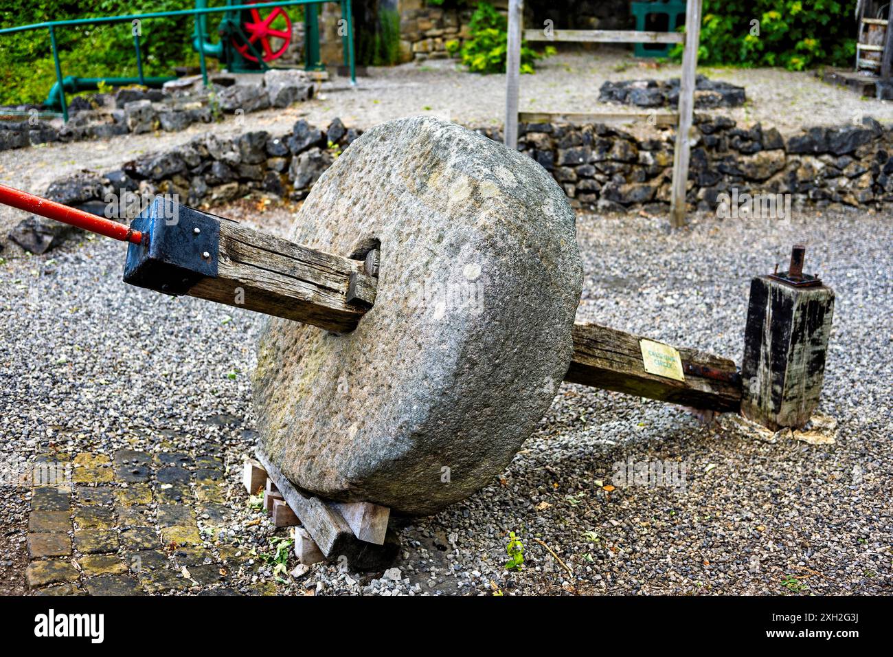 Alte Mühlsteine auf einem rustikalen Stand im Freien, mit historischen Fräsmaschinen in ländlicher Umgebung. Stockfoto