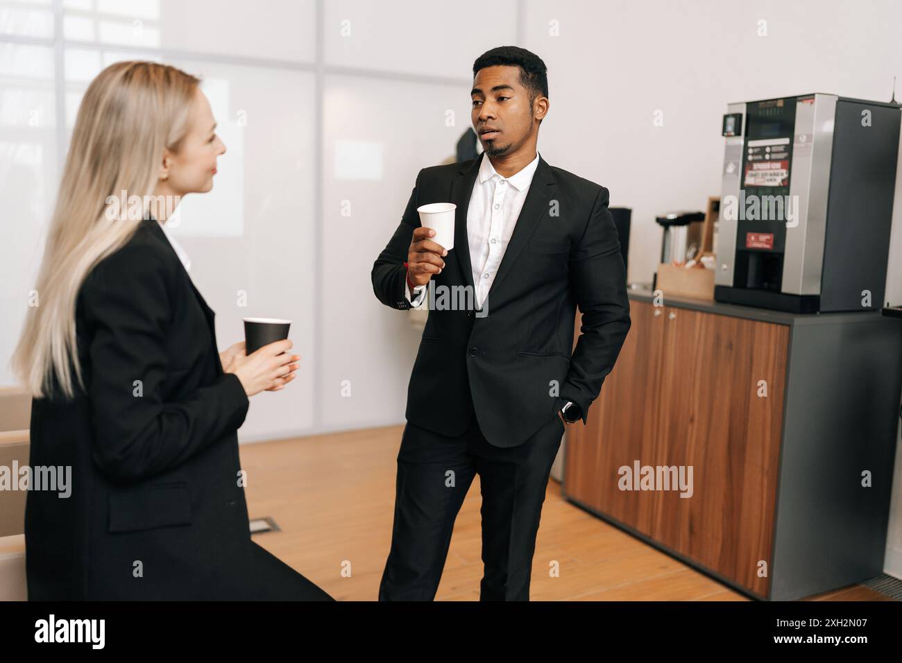 Verschiedene Geschäftsleute im Anzug, die eine Kaffeepause machen und sich im Büro unterhalten. Glückliche männliche weibliche Angestellte genießen Kaffeepause drinnen. Stockfoto