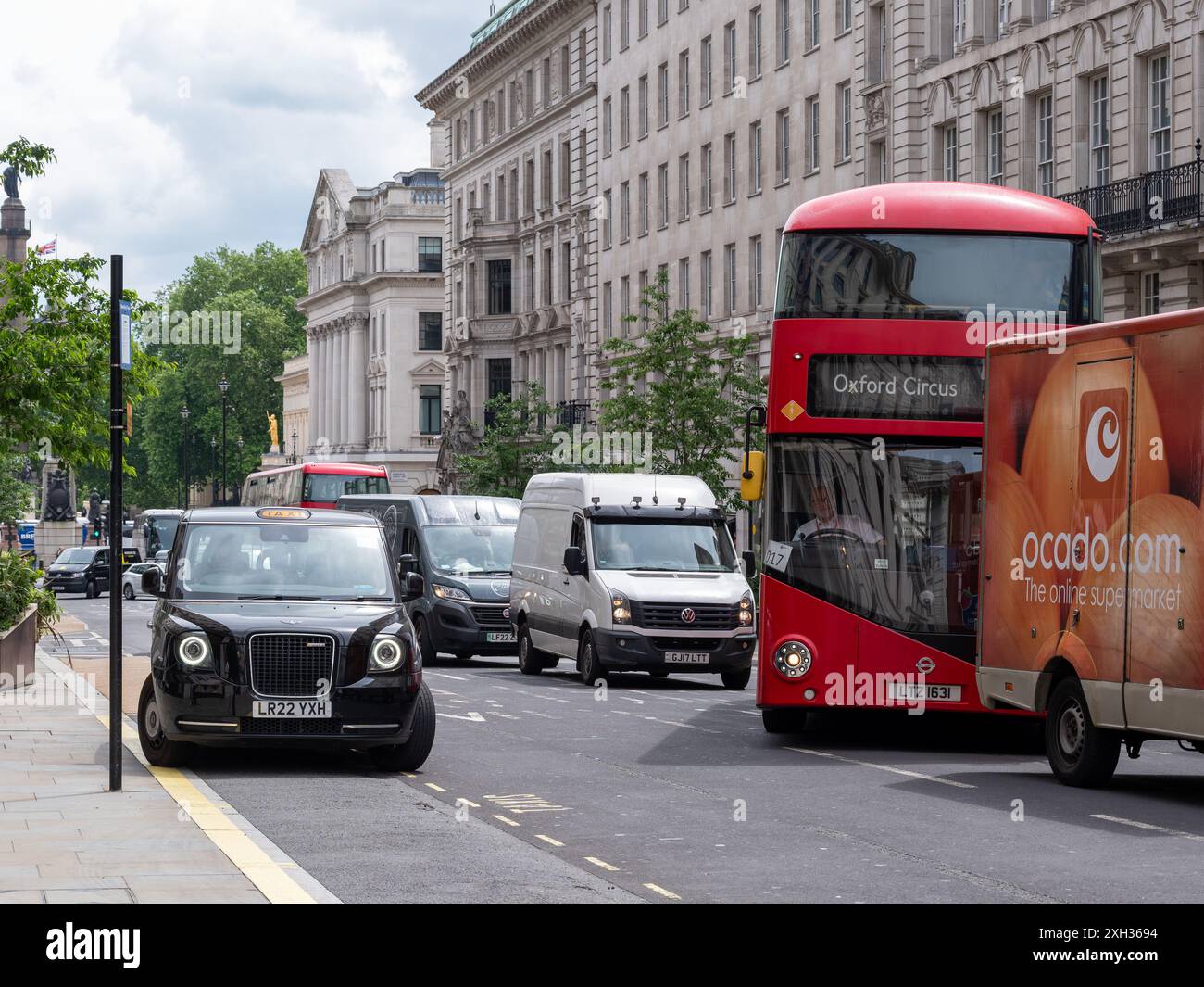 London, England - 02. Juni 2024: Londoner Verkehr mit geparktem schwarzen Taxi und rotem Stadtbus, der in der Hauptverkehrszeit die Fahrspur wechselt Stockfoto