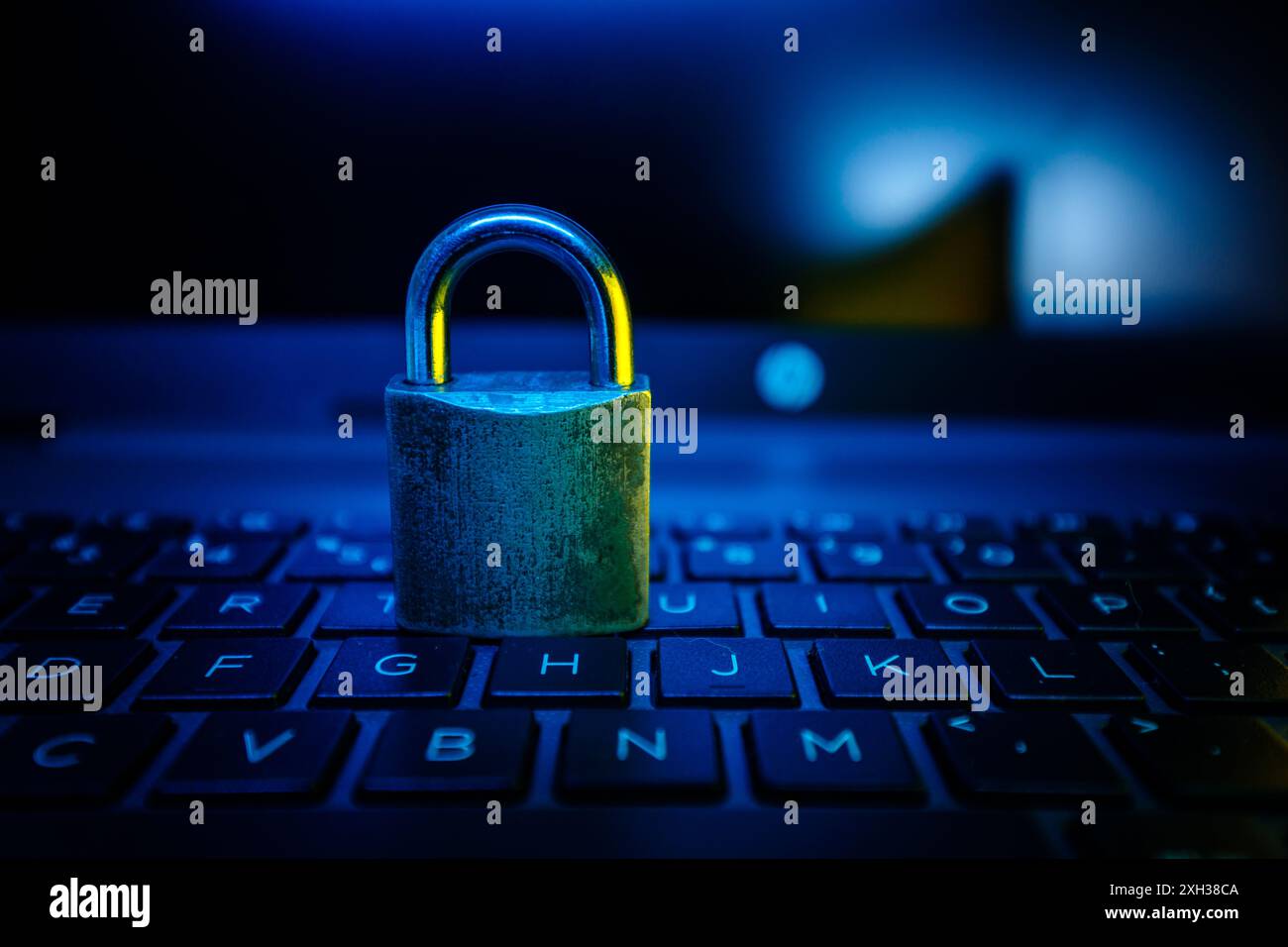 Ein silbernes Vorhängeschloss befindet sich auf einer Laptop-Tastatur, die von blauem Licht beleuchtet wird. Stockfoto