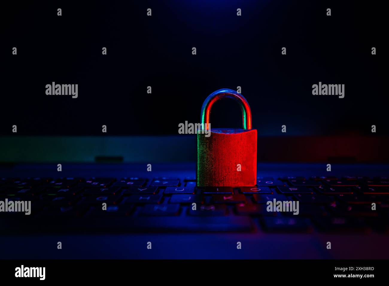 Ein geschlossenes Vorhängeschloss befindet sich auf einer dunklen Laptop-Tastatur, die von rotem und blauem Licht beleuchtet wird. Stockfoto