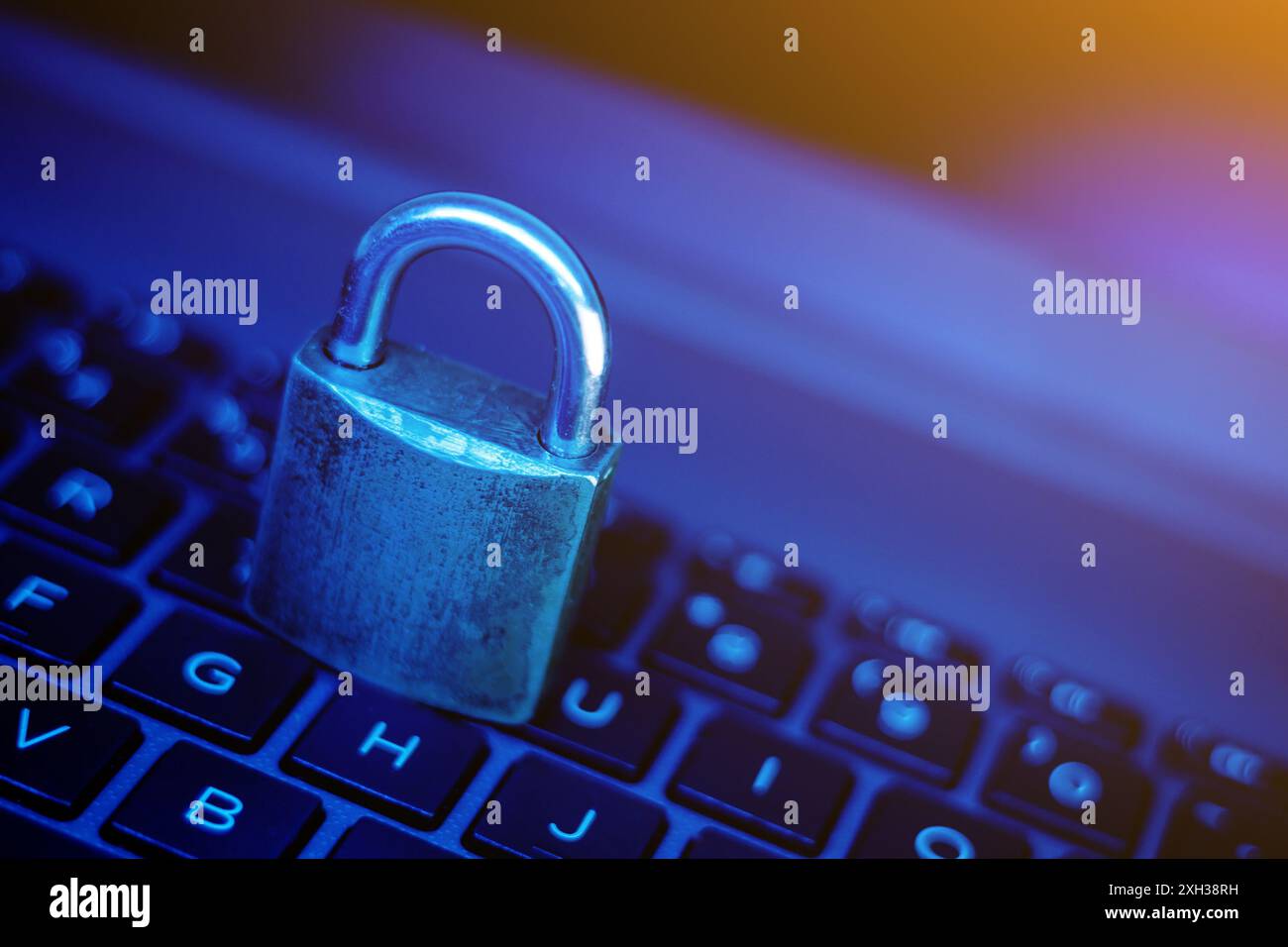 Ein Vorhängeschloss aus Metall sitzt auf den Tasten einer Laptop-Tastatur. Das Bild wird blau beleuchtet. Stockfoto