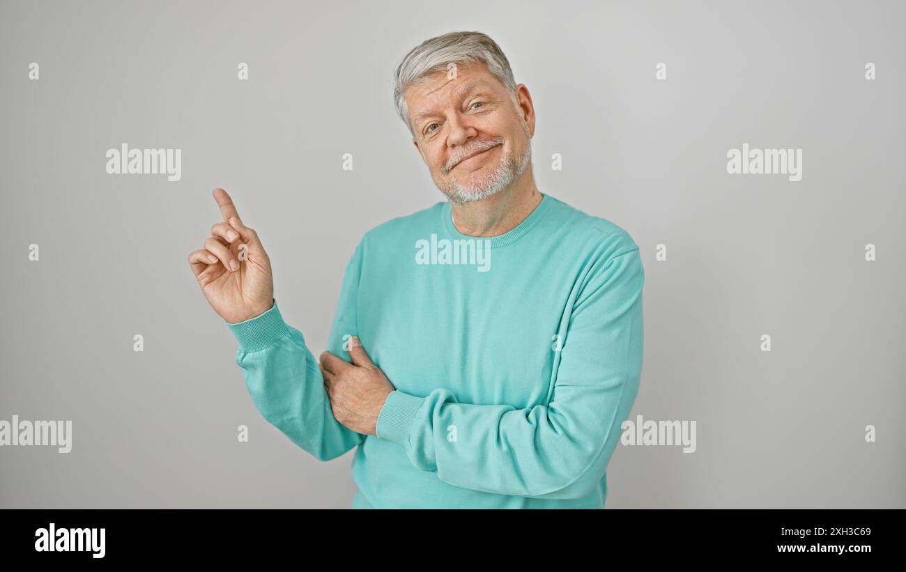 Lächelnder älterer Mann in türkisfarbenem Pullover isoliert auf weißem Hintergrund, der mit Zeigefinger zeigt Stockfoto