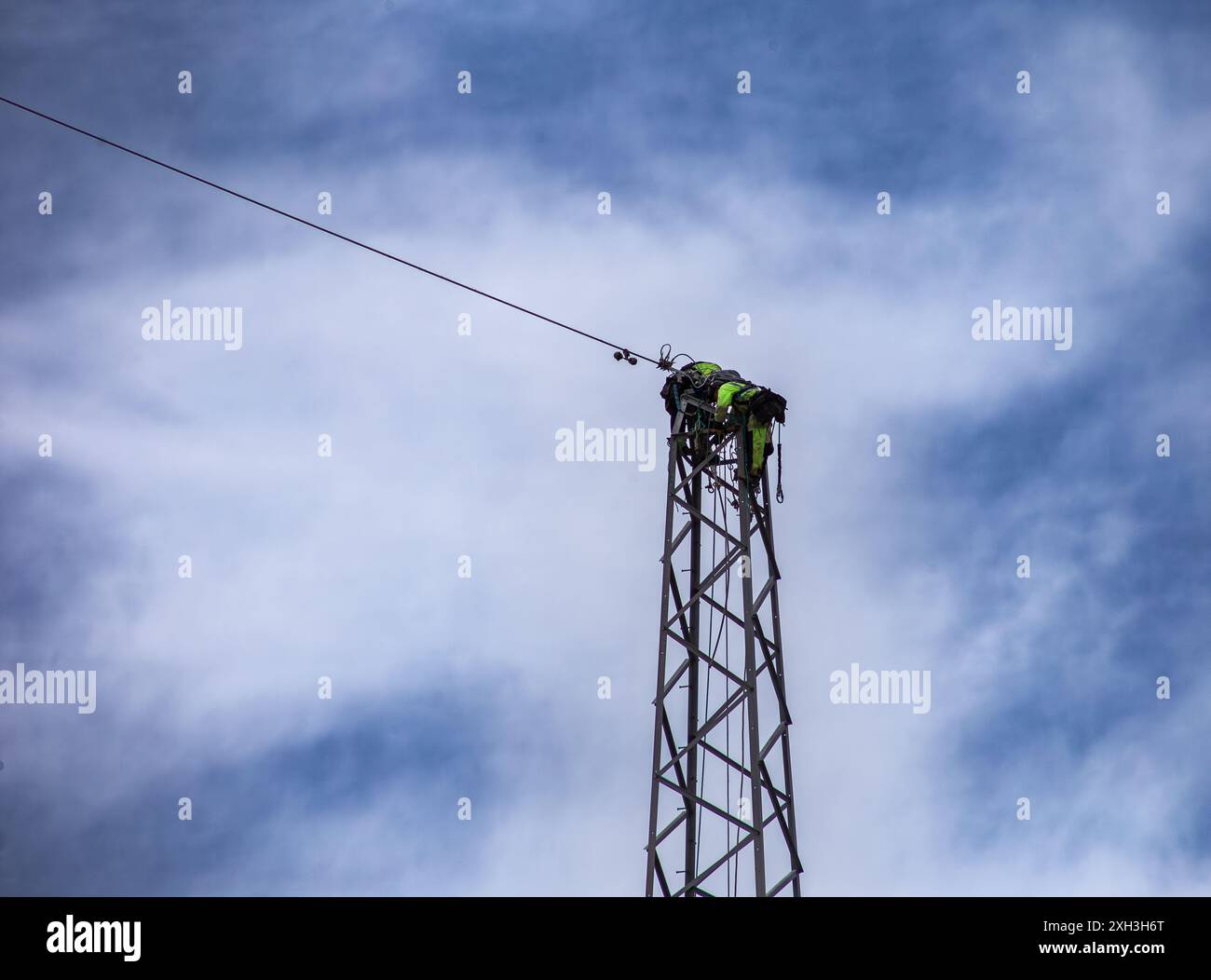 Arbeiter in gut sichtbarer Kleidung auf einem elektrischen Pylonturm vor bewölktem Himmel Stockfoto
