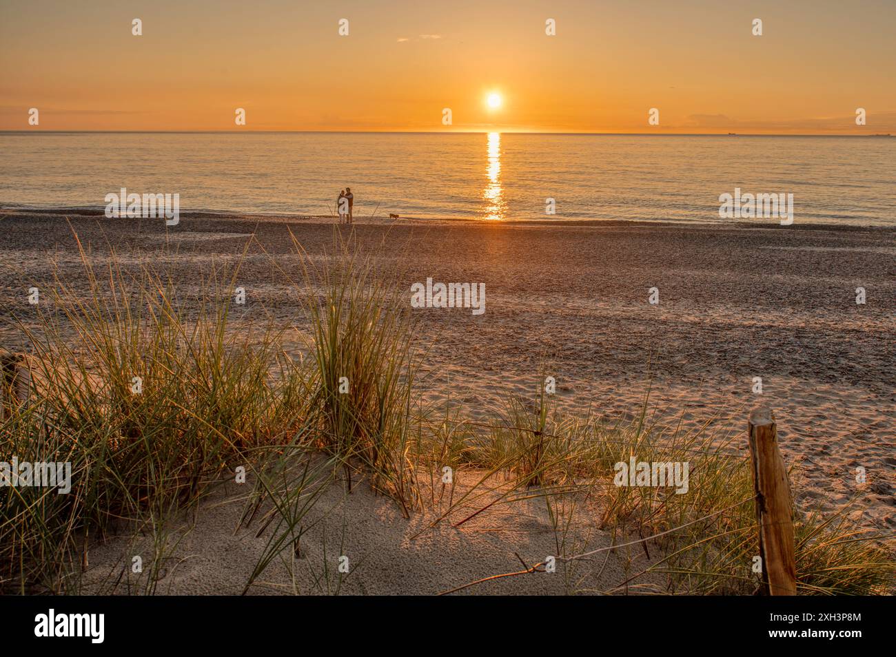Ein Paar am Strand bei Sonnenuntergang und Dünen mit einem Drahtzaun im Vordergrund, Skagen, Dänemark, 30. Mai 2024 Stockfoto