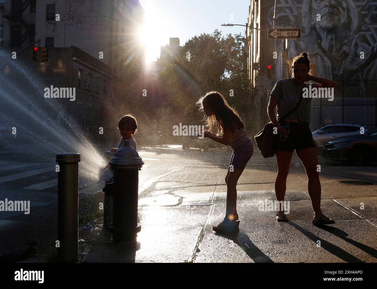 New York, Usa. Juli 2024. Ein Erwachsener und zwei Kinder halten am Donnerstag, den 11. Juli 2024, an einem offenen Hydranten an, um sich bei heißem und feuchtem Wetter in New York City abzukühlen. Nach der extremen Luftfeuchtigkeit und Hitze der letzten Tage bekam die Gegend eine Pause, da die Luftfeuchtigkeit leicht, aber spürbar abnahm. Foto: John Angelillo/UPI Credit: UPI/Alamy Live News Stockfoto