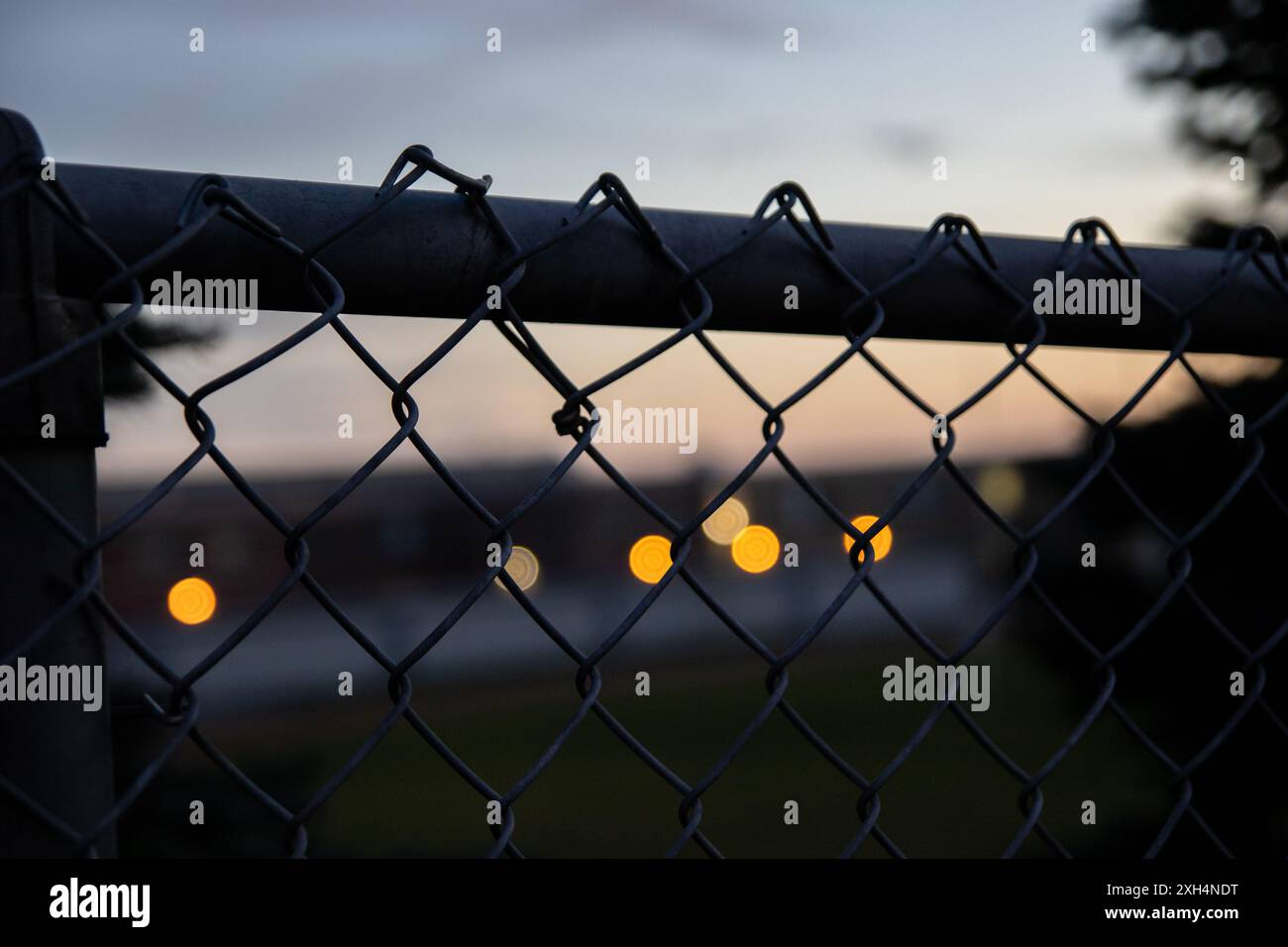 Bokeh-Lichter bei Sonnenuntergang hinter Maschendrahtzaun - verschwommener urbaner Hintergrund mit warmen glühenden Kugeln - Sonnenuntergang. Aufgenommen in Toronto, Kanada. Stockfoto