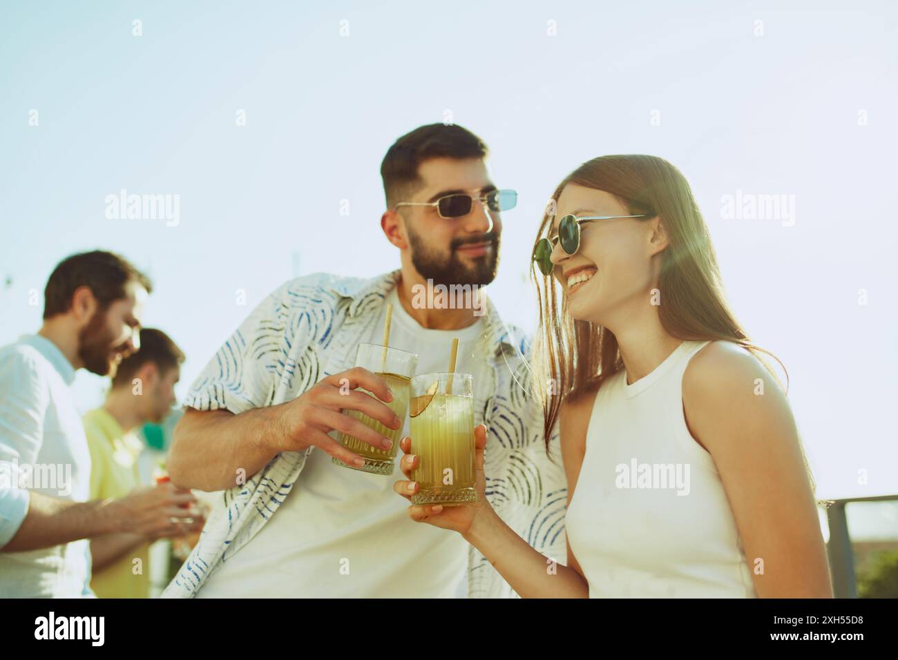Junge Erwachsene Menschen, Freunde, teilen Momente der Feier, heben ihre Getränke, Cocktails hoch in jubelnden Toast unter der Sonne. Stockfoto