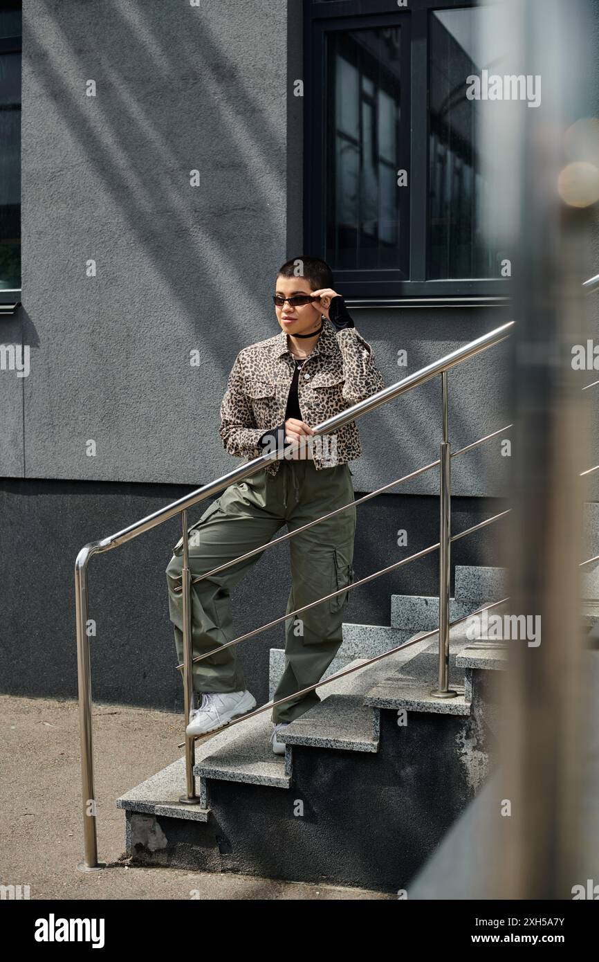 Eine junge Frau in stilvoller Kleidung steht auf der Treppe neben dem modernen Gebäude. Stockfoto