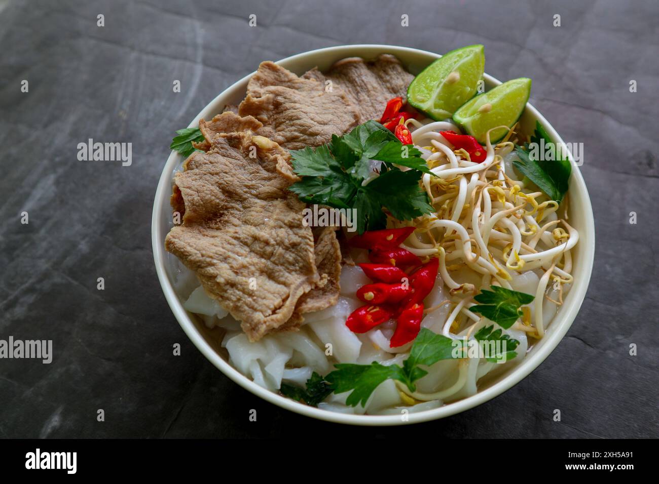 Eine Schüssel Pho Bo traditionelle Suppe mit Rindfleisch, Reisnudeln, Ingwer, Limette, Chili in einer Schüssel. Nahaufnahme. Vietnamesische Küche auf schwarzem Hintergrund Stockfoto