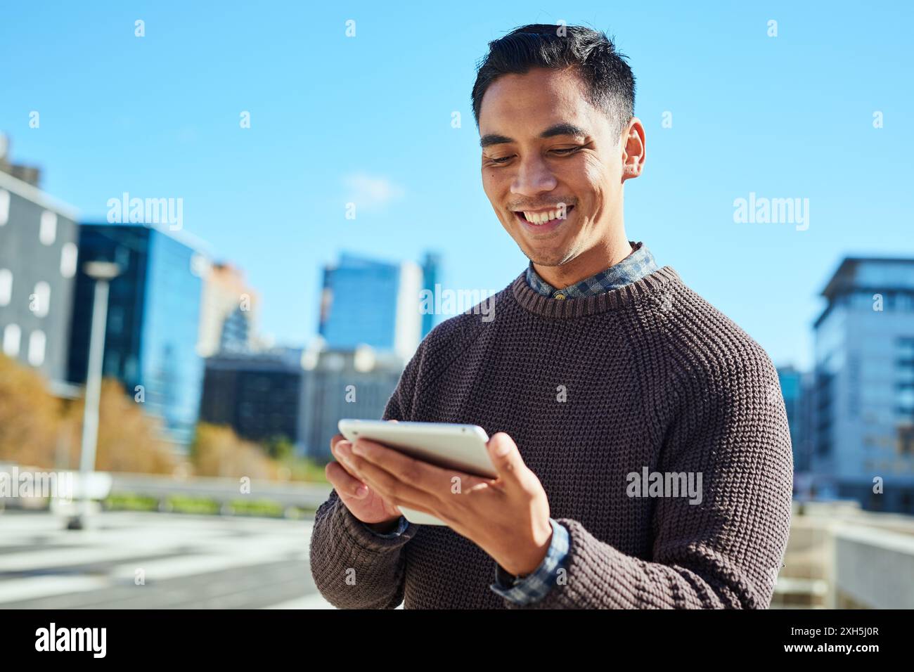 Lächelnder junger Profi, der ein Tablet in der städtischen Umgebung mit der Skyline der Stadt im Hintergrund verwendet Stockfoto