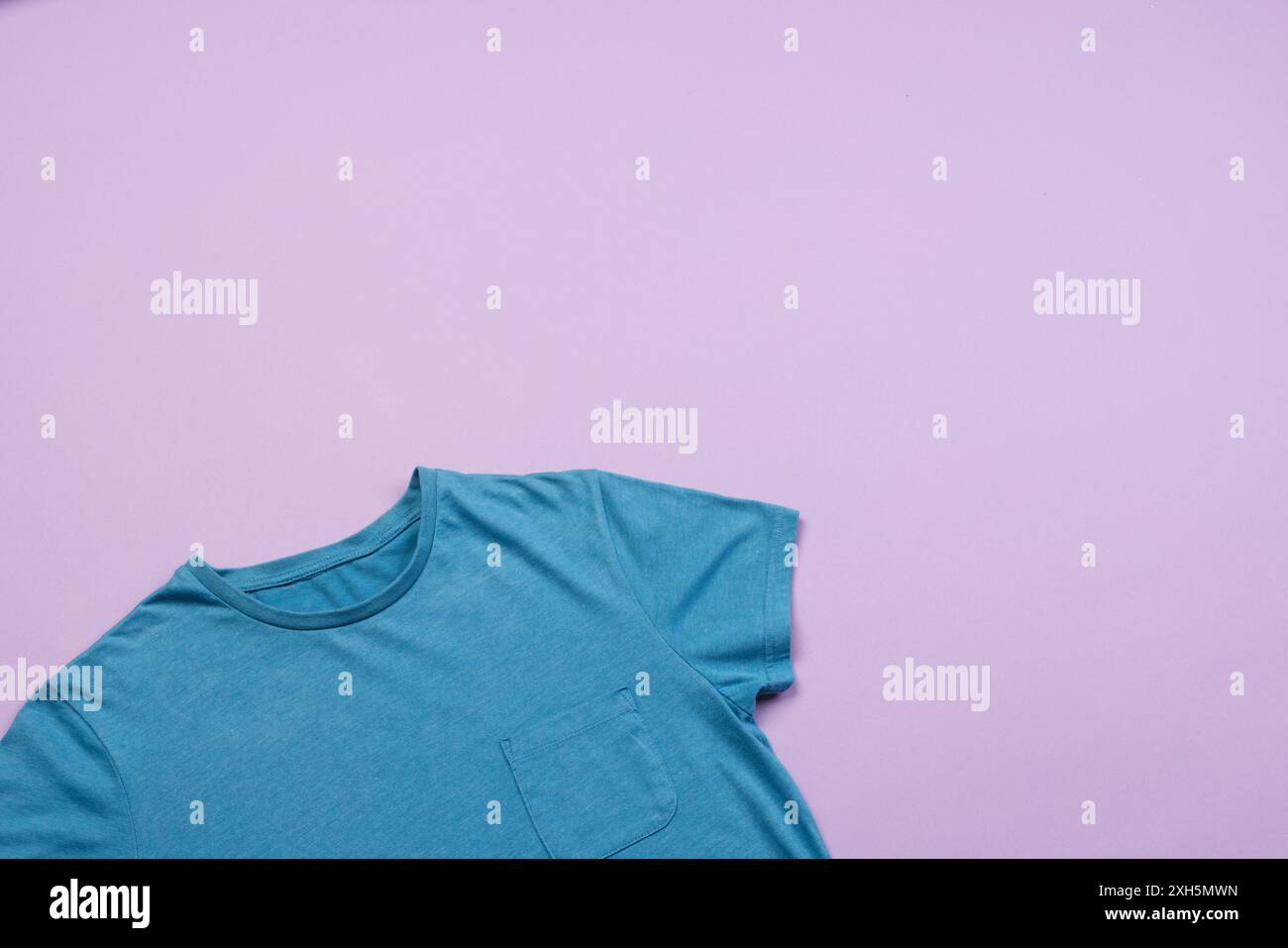 Ein blaues T-Shirt ist auf einem violetten Hintergrund mit Platz für Kopien angeordnet. Das schlichte Design eignet sich ideal für grafische Drucke oder Logos für das Branding von pur Stockfoto