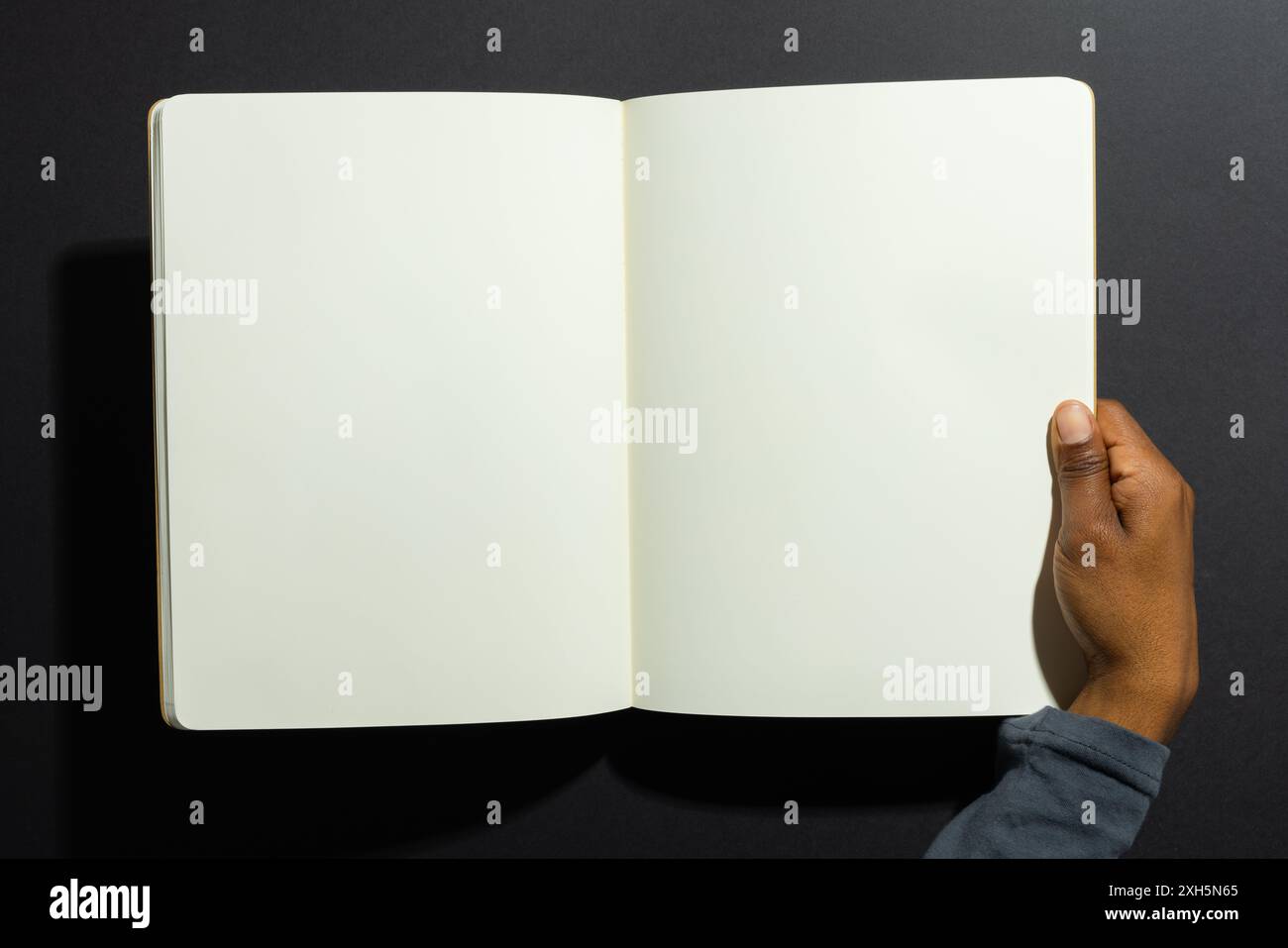 Afroamerikanische Hand, die ein offenes leeres Notizbuch hält, mit Kopierraum. Ideal für die Präsentation von Text- oder Grafikinhalten in einem Bildungskontext. Stockfoto