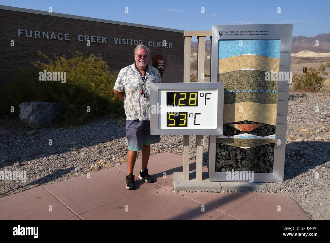 Jay Christensen von Sherman Oaks, Kalifornien, posiert mit dem Thermometer im Furnace Creek Visitor Center, das 128 Grad Fahrenheit (53 Grad Celsius) in de anzeigt Stockfoto