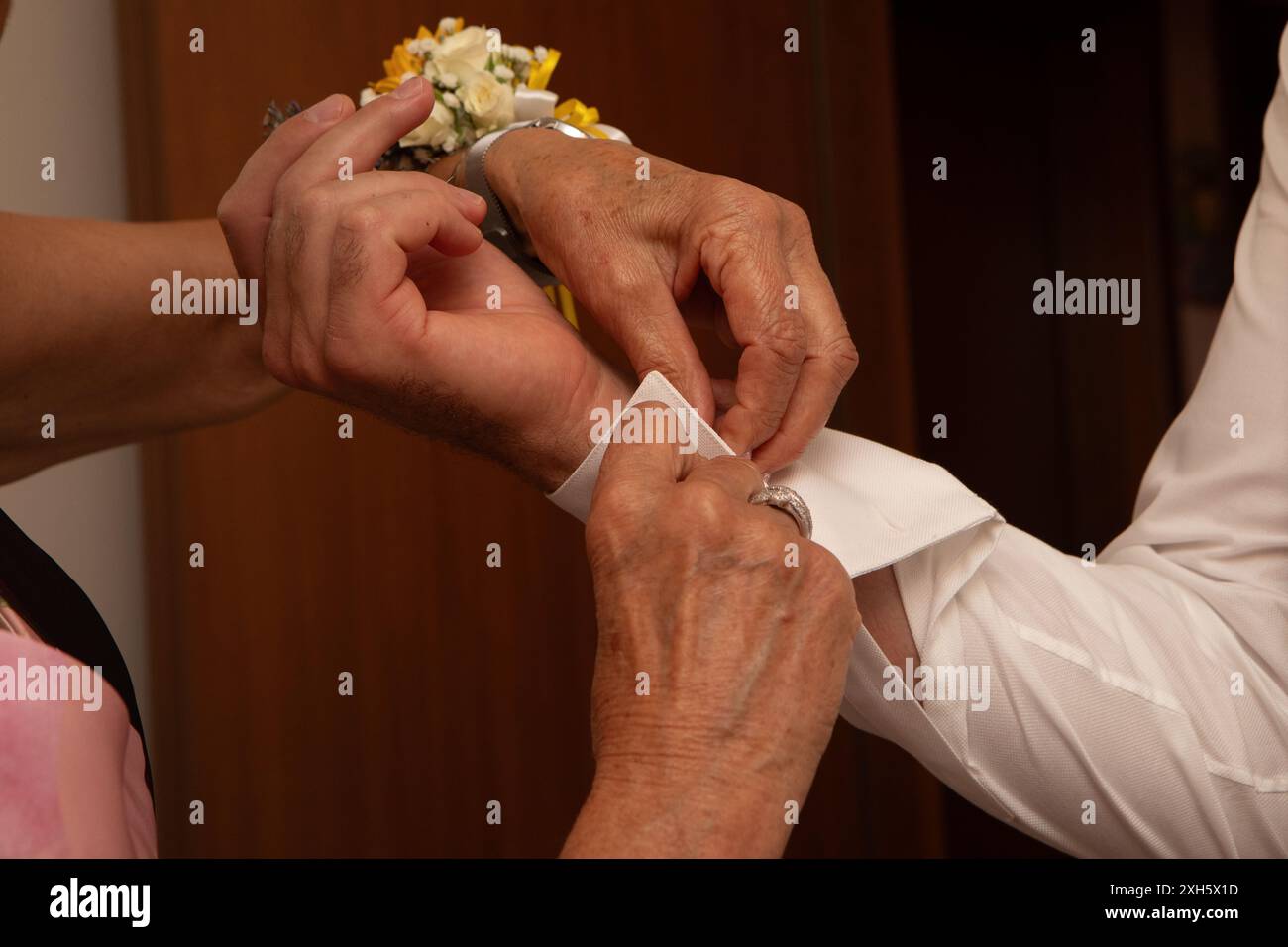 Die Frau hilft einem Bräutigam, seine weiße Hemdmanschette zu knöpfen, während er sich auf seine Hochzeit vorbereitet Stockfoto