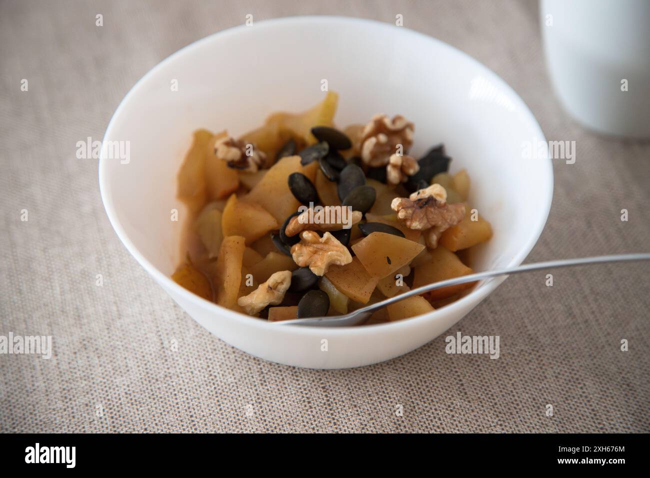 Schüssel gebackener Apfel mit Zimt, Walnüssen und Kürbiskernen, gesundes Frühstück auf einer beigen Tischdecke. Stockfoto