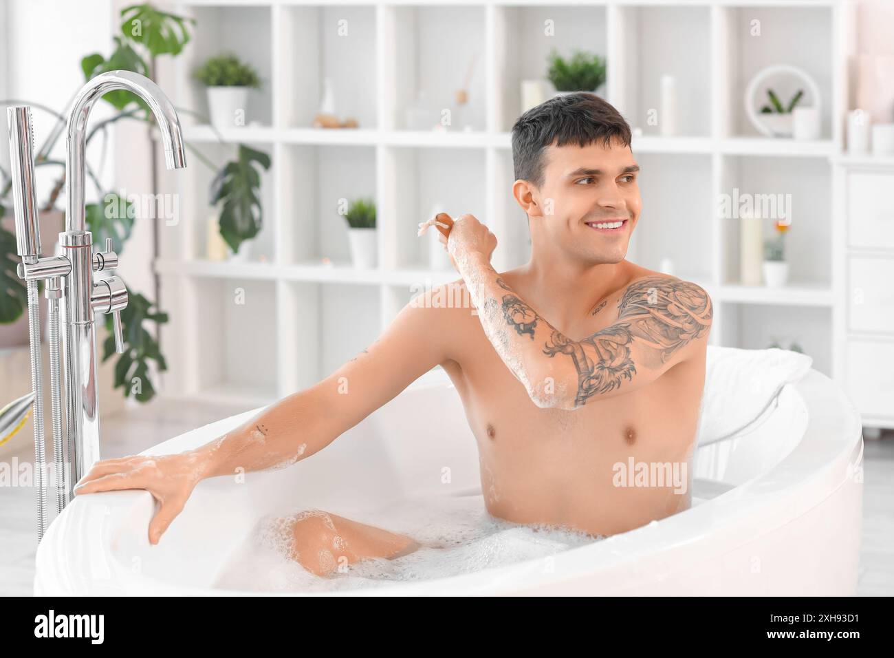 Hübscher junger Mann, der sich zu Hause in der Badewanne den Rücken massiert Stockfoto
