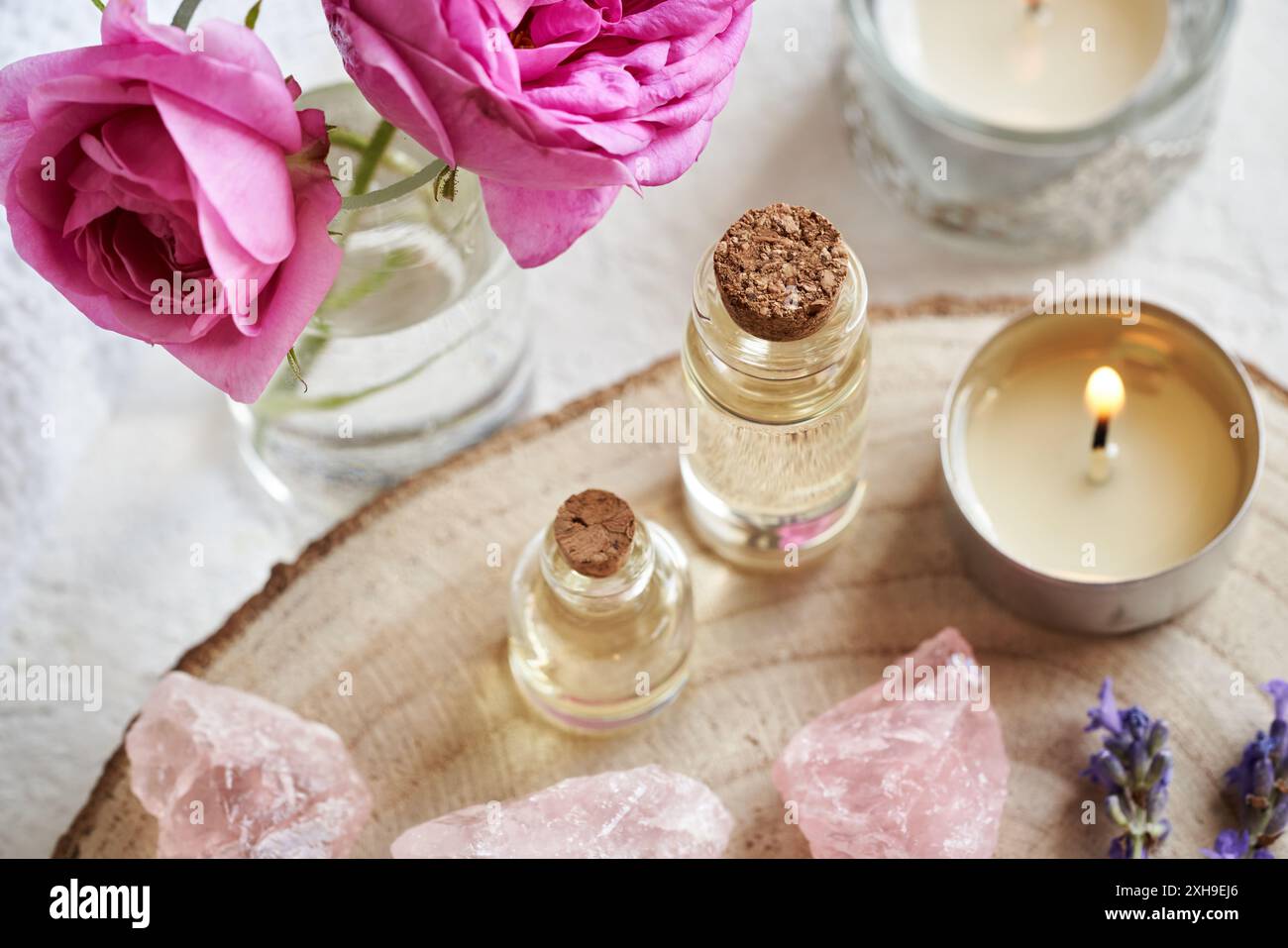 Flaschen mit ätherischen Ölen mit Kohlrosen- und Lavendelblüten und Rosenquarzsteinen Stockfoto