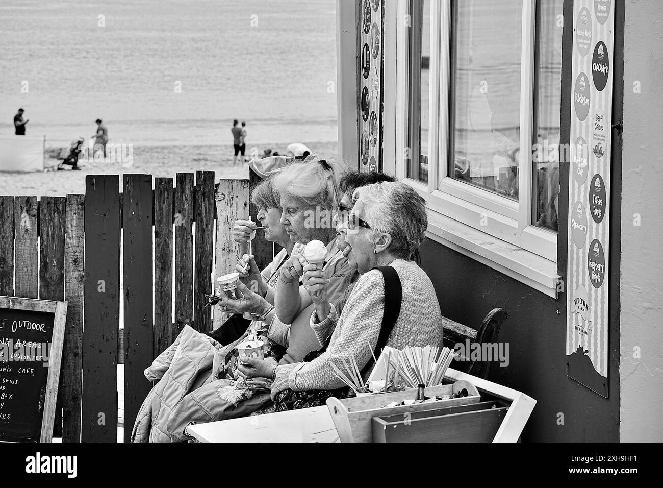 Tenby, Pembrokeshire, Wales - 2. Juli 2024: Vier ältere Damen sitzen auf einer Bank neben South Beach und genießen gemeinsam ein Eis. Stockfoto