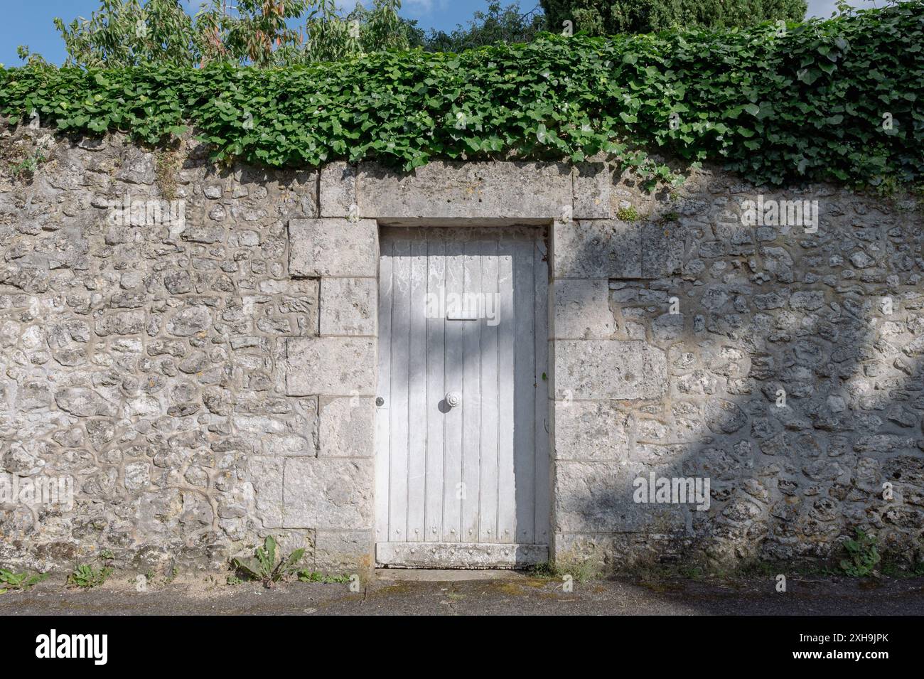 Eine weiße Tür in einer hohen Steinmauer, die einen Garten umgibt. Aufgenommen an sonnigen Sommertagen ohne Menschen Stockfoto