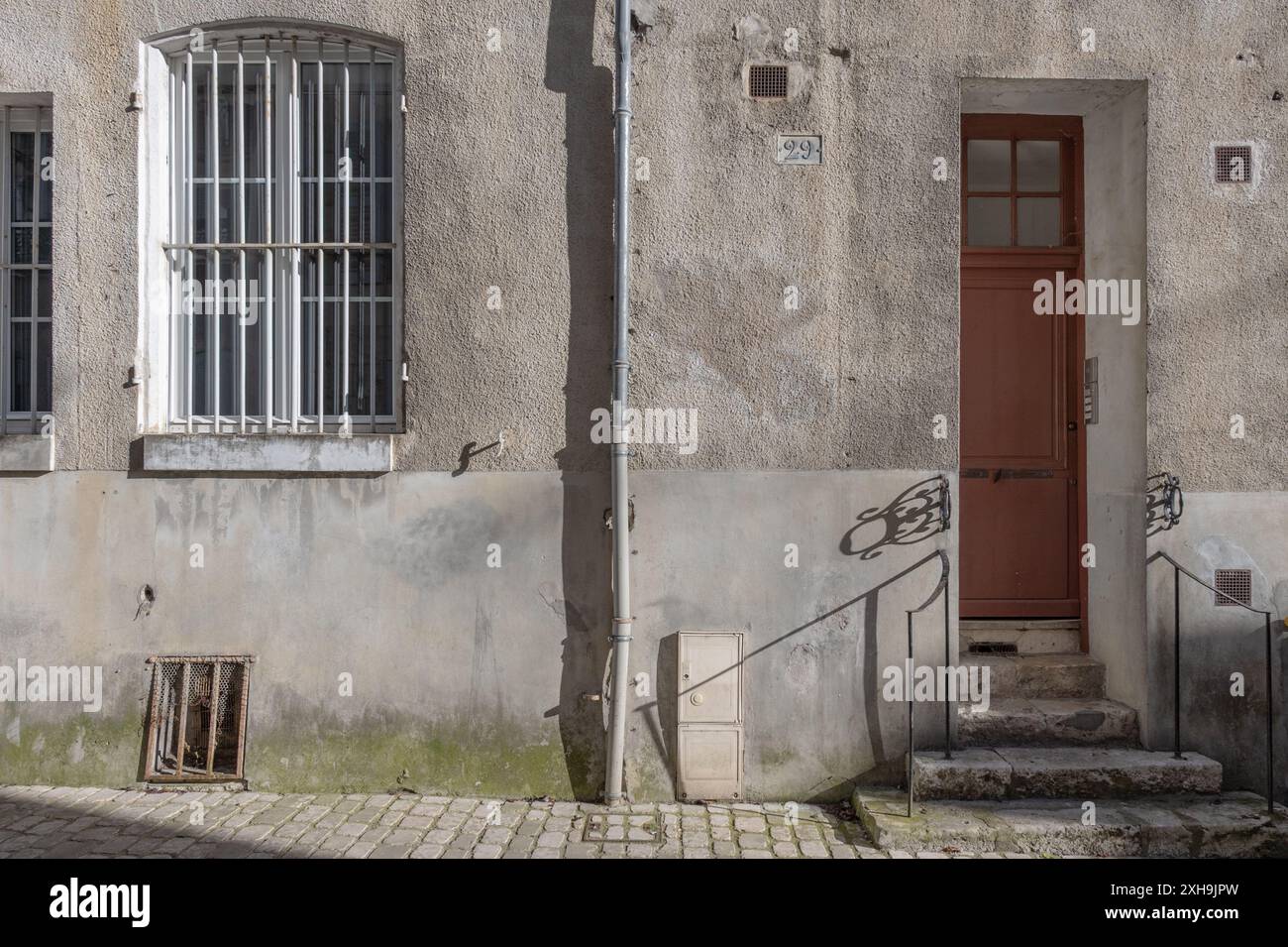Die Fassade eines alten französischen Hauses mit einer roten Eingangstür. Aufgenommen an einem sonnigen Sommerabend mit Schattenmustern und ohne Leute. Stockfoto