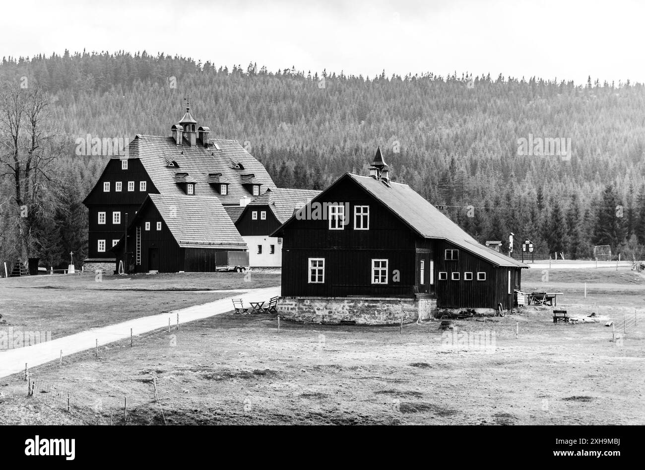 Ein Schwarzweiß-Foto, das die historischen Häuser des Dorfes Jizerka darstellt, eingebettet in das malerische Isergebirge in Tschechien. Die Gebäude verfügen über eine traditionelle Architektur mit dunklen Holzfassaden und geneigten Dächern. Stockfoto