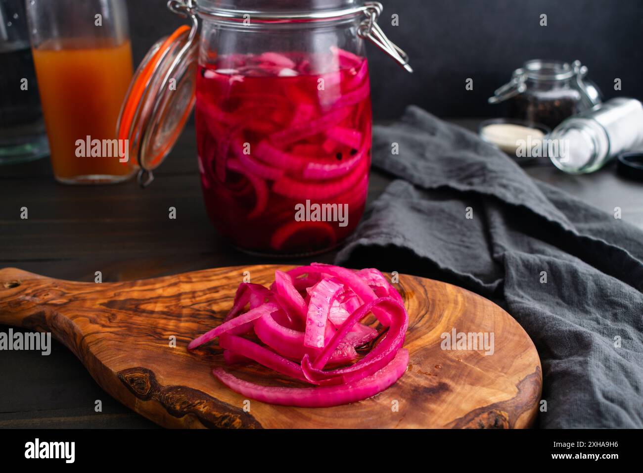 Nahansicht eingelegter Zwiebeln auf einem Schneidebrett: In hellen Farben geschnittene rote Zwiebeln, eingelegt in einem einmauerglas, umgeben von Zutaten Stockfoto
