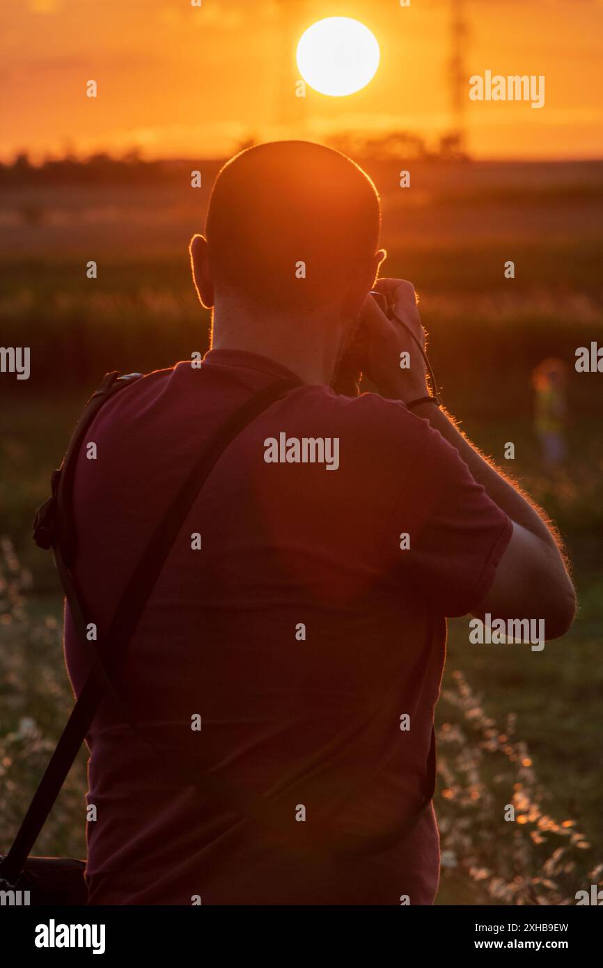 Fänger der Sonne. Fotograf, der den Sonnenuntergang einfängt, von hinten aufgenommen. Stockfoto