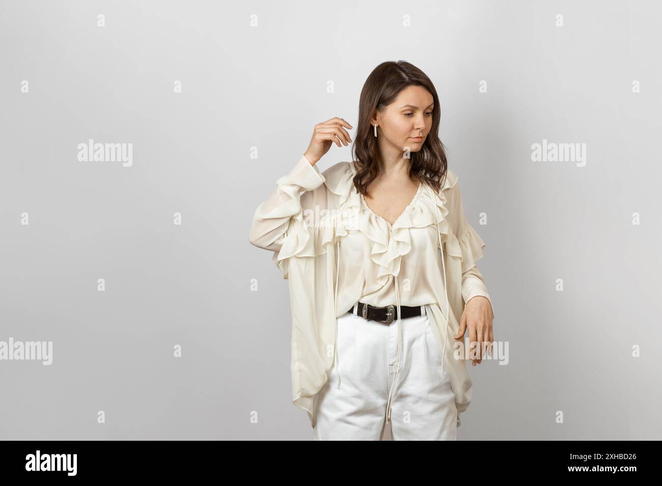 Eine stilvolle Frau in einer weißen Rüschenbluse und einer weißen Hose steht anmutig. Perfekt für Mode- und Lifestyle-Themen. Stockfoto