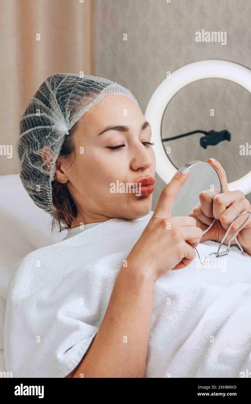 Die Frau beobachtet sorgfältig die Auswirkungen ihrer neuesten Hautpflege und untersucht ihren erfrischten Teint mit einem Spiegel Stockfoto