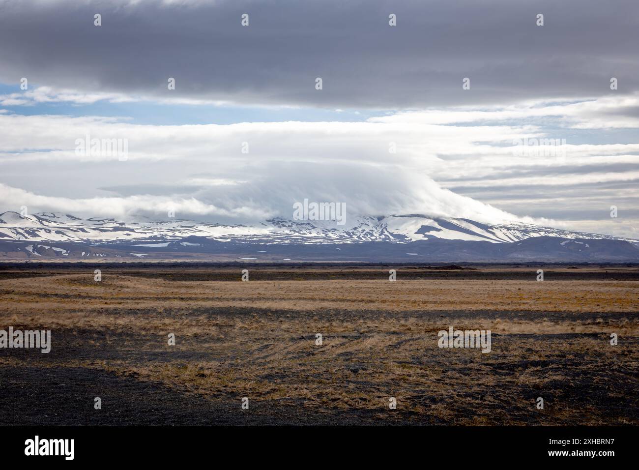 Rohe isländische Landschaft mit Grasland, Lavafeldern und schneebedecktem Hekla-Vulkan mit Wolken. Stockfoto