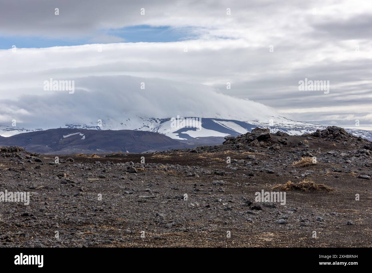 Rohe isländische Landschaft mit vulkanischem Lavafeld und schneebedecktem Hekla-Vulkan mit Wolken. Stockfoto