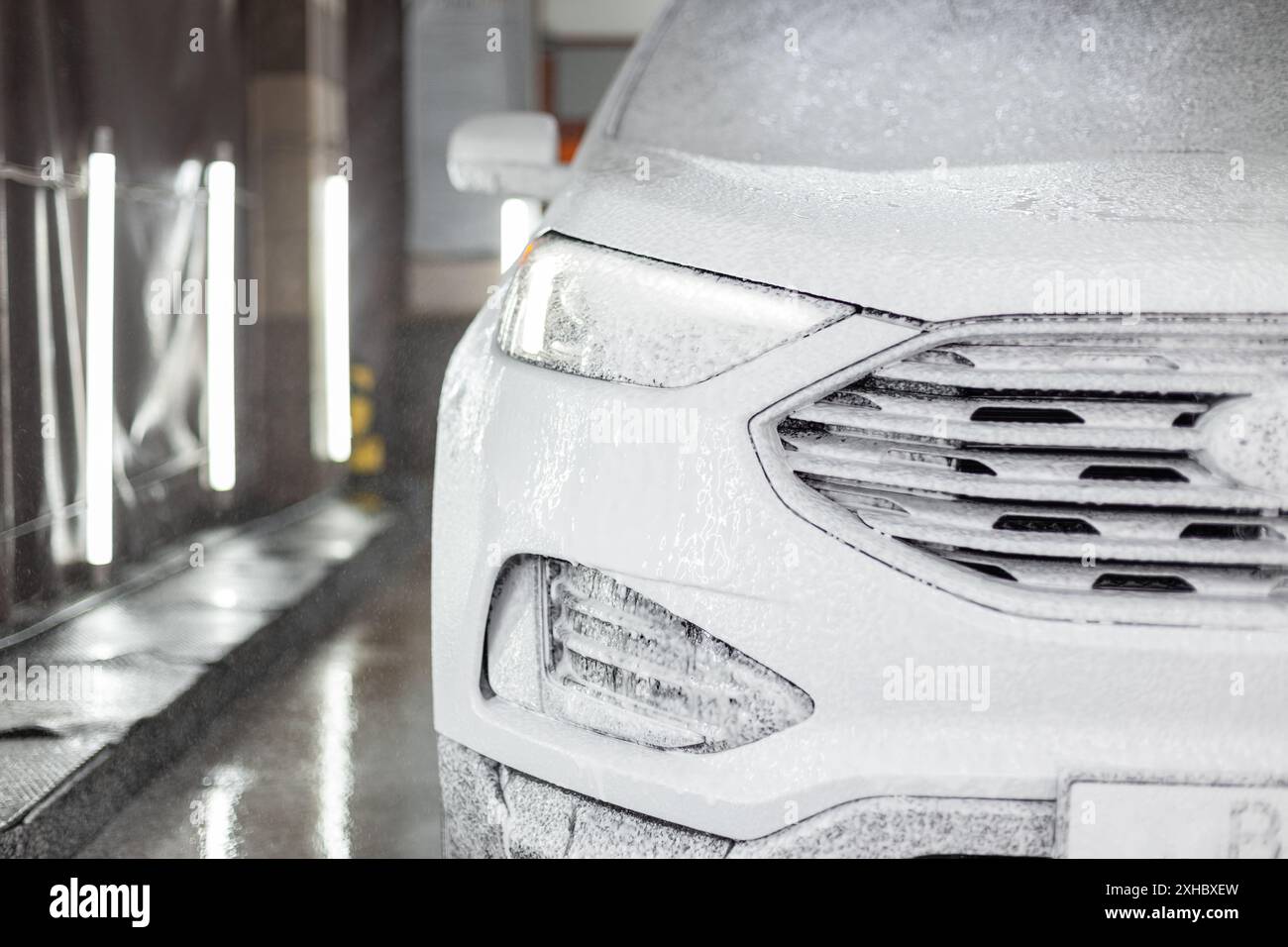 Modernes Auto im Shampoo-Schaum in einer Autowaschanlage. Autowäsche und -Pflege Stockfoto