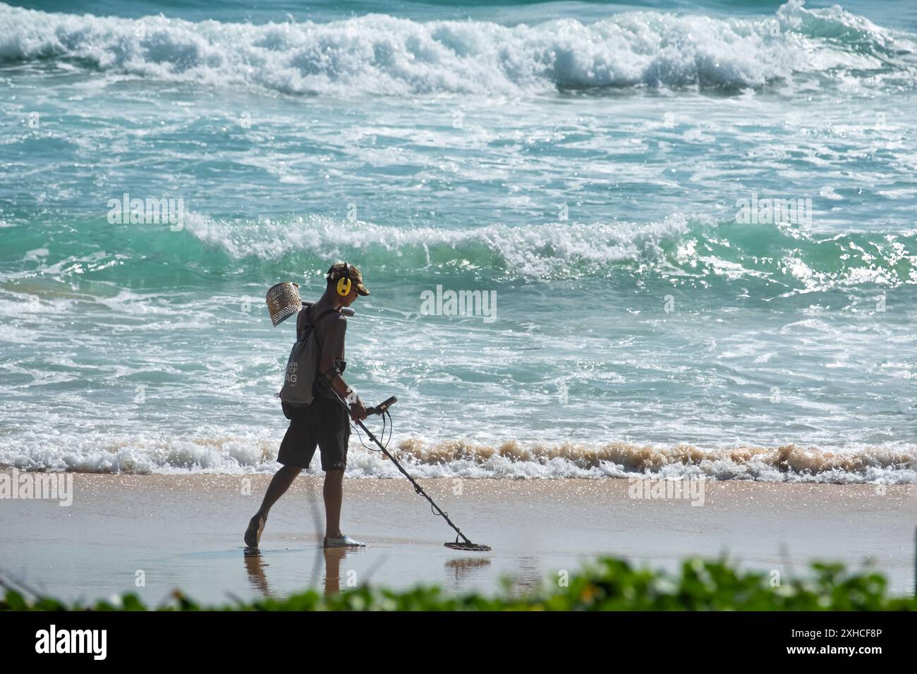 Junger Mann mit Metalldetektor, der den Sandstrand an einem sonnigen Sommertag in Phuket Thailand sucht. Schmuck am Strand mit dem Metalldetektor finden. T Stockfoto