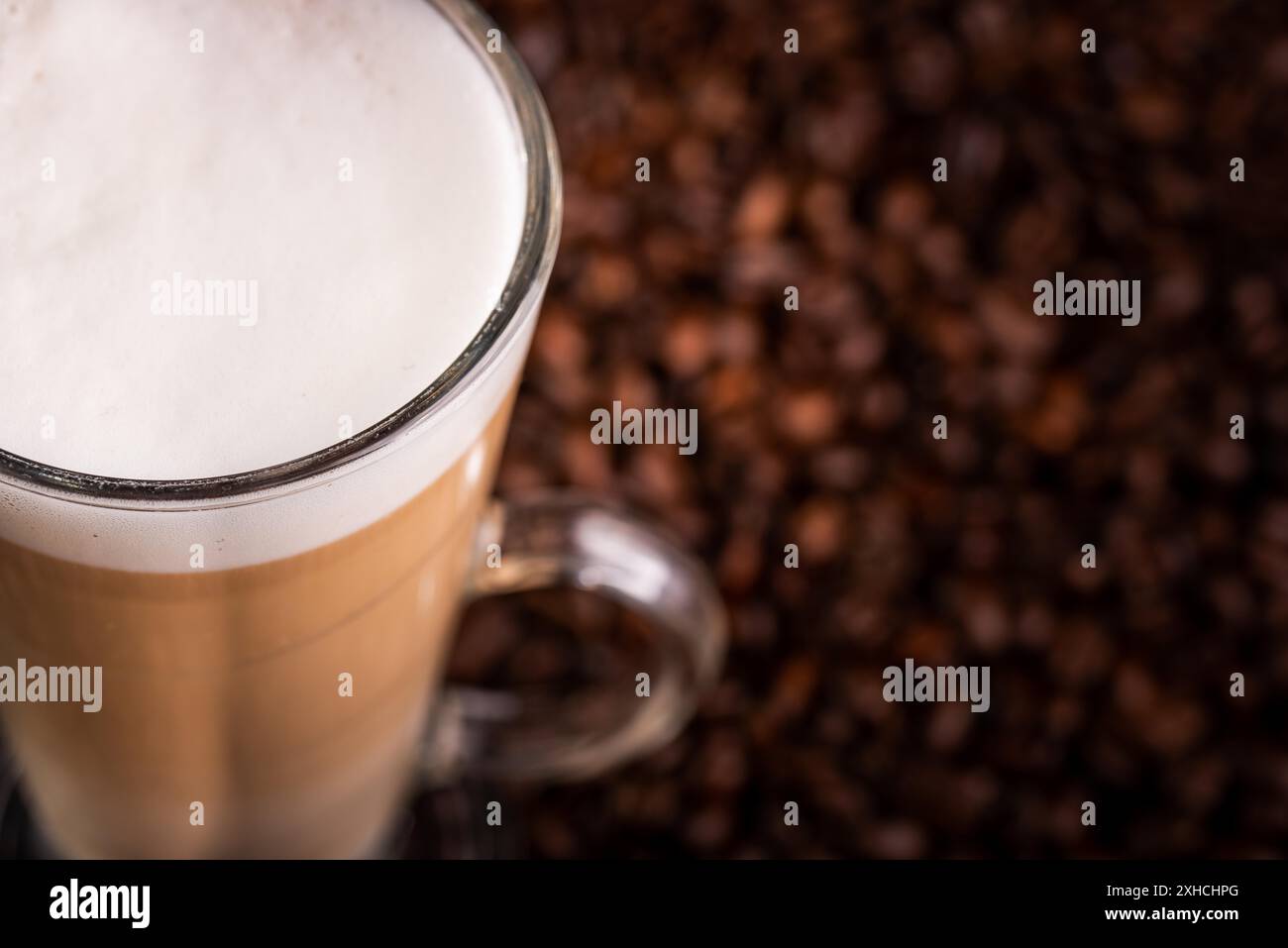 Kaffee Latte mit schaumiger Milch in hohem Glas, auf Kaffeebohnen auf schwarzem Hintergrund. Blick von oben Stockfoto