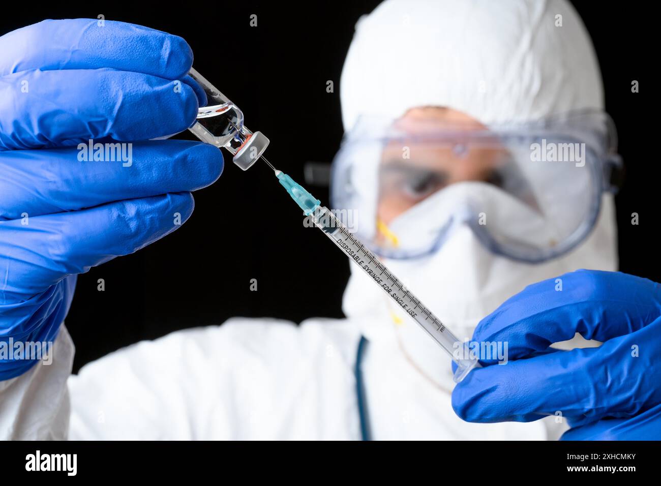 Arzt oder Wissenschaftler in PPE-Suite Uniform im Labor halten Medizin Flüssigkeit Impfstoff Fläschchen und Spritze auf schwarzem isolierten Hintergrund Stockfoto