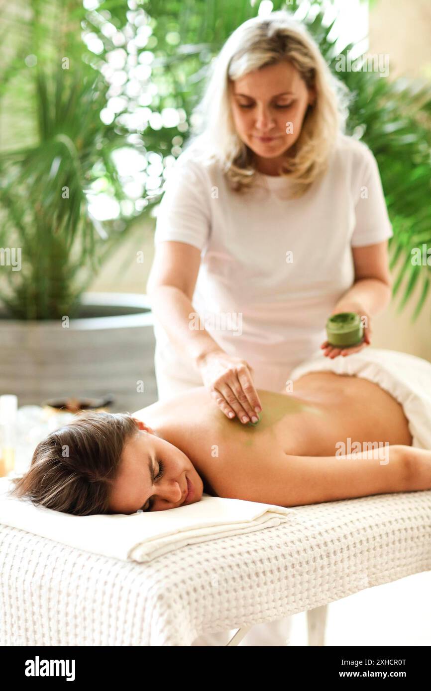 Schöne entspannte Frau mit Tonmaske Anwendung auf den Rücken im Spa-Salon Stockfoto