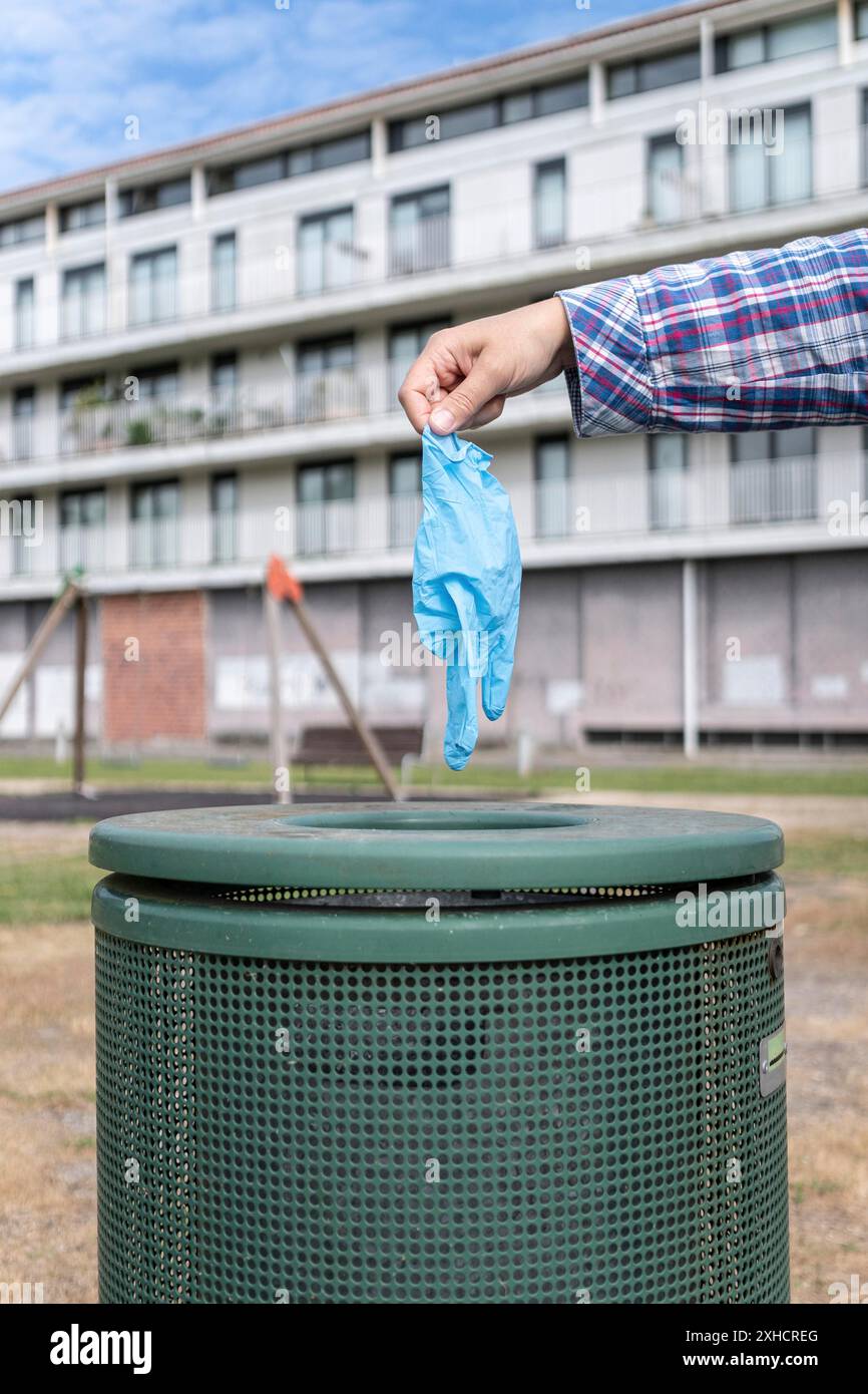 Weibliche Hand wirft Schutzhandschuh in den Mülleimer eines Parks. Coronavirus oder Covid-19 Abfallkonzept Stockfoto