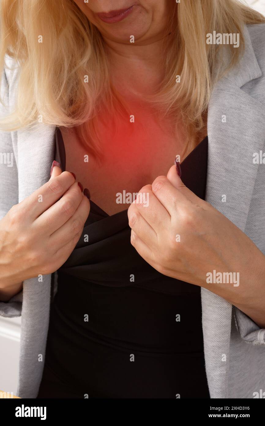 Wechseljahre. Frau bläst Luft auf sich, um sich während des heißen Blitz am Tisch in der Küche abzukühlen Stockfoto
