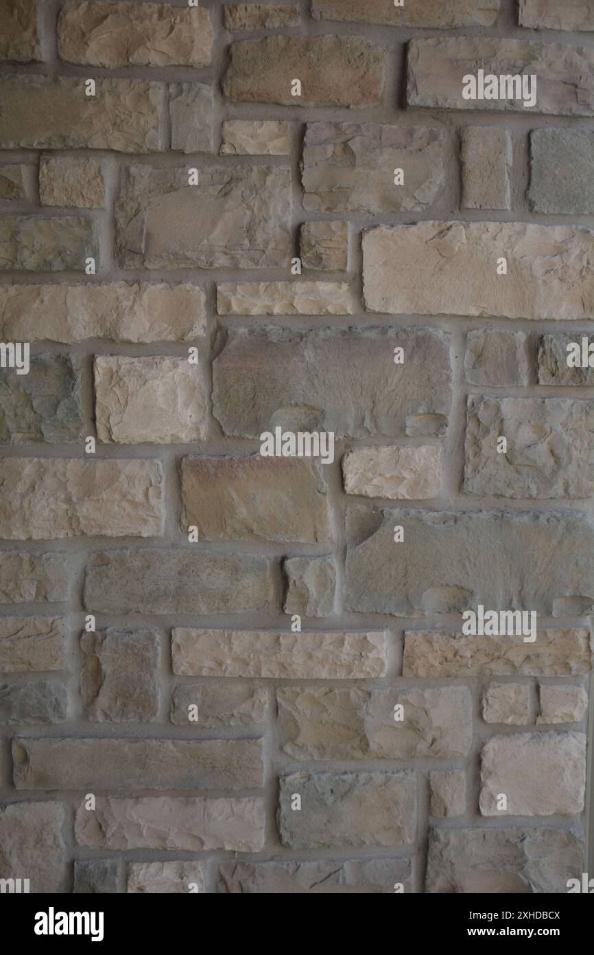 Nahaufnahme einer quadratischen grauen Steinmauer mit Elementen in braunen, gelben, orangen und cremefarbenen Erdtönen. Stockfoto