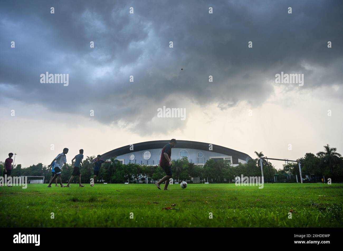 Noida, Indien. Juli 2024. NOIDA, INDIEN - 13. JULI: Menschen spielen Fußball unter dunklen Wolken nach einem frühen Morgenregen im Noida-Stadion am 13. Juli 2024 in Noida, Indien. Starke Regenfälle in Teilen von Delhi-NCR verursachten in vielen Gegenden große Wasserabfälle, wodurch Bewohner und Pendler gestrandet waren und einen riesigen Stau verursachten. In vielen Gebieten hat die Wassereinschlagung dazu geführt, dass Buslinien umgeleitet werden. (Foto: Sunil Ghosh/Hindustan Times/SIPA USA) Credit: SIPA USA/Alamy Live News Stockfoto