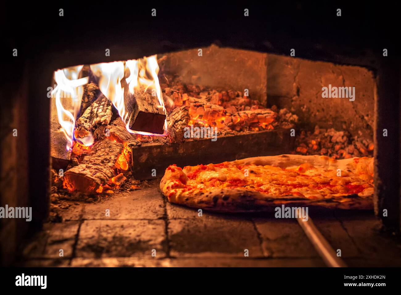 Eine einzelne Pizza kocht in einem Backofen mit einem brausenden Feuer und glühender Glut. Stockfoto