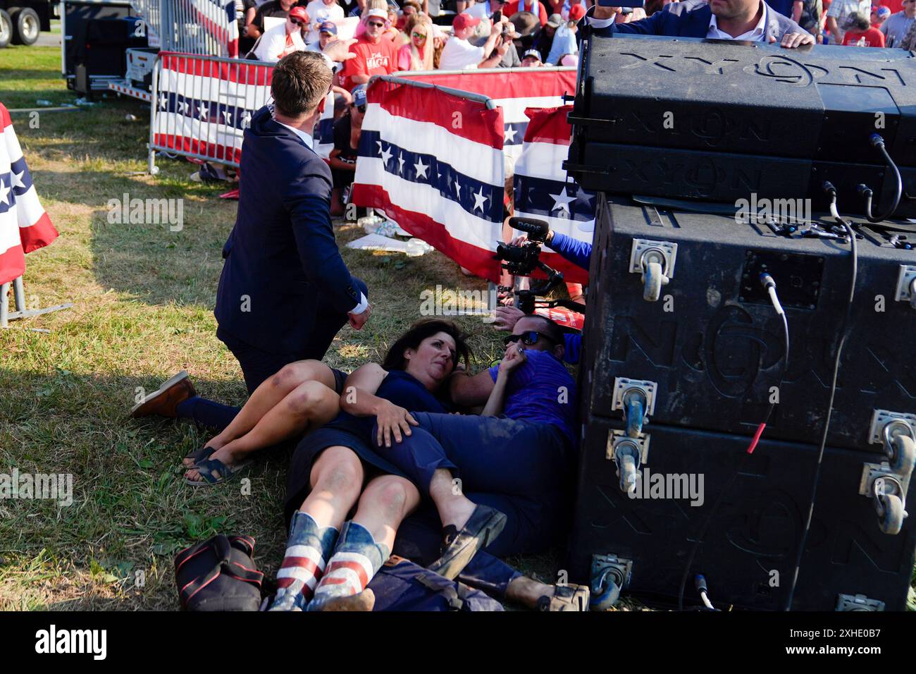 People take cover as U.S. Secret Service agents surround Republican presidential candidate former President Donald Trump on stage at a campaign rally, Saturday, July 13, 2024, in Butler, Pa. (AP Photo/Evan Vucci) Stockfoto